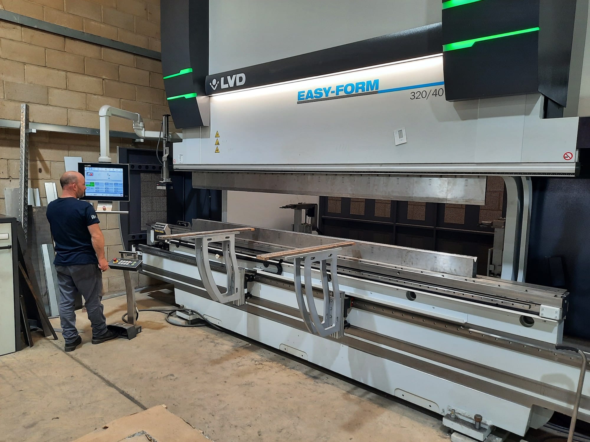 Operator using a large CNC press brake to bend metal at Riteweld Engineering’s workshop, with control panel and metal sheet visible.