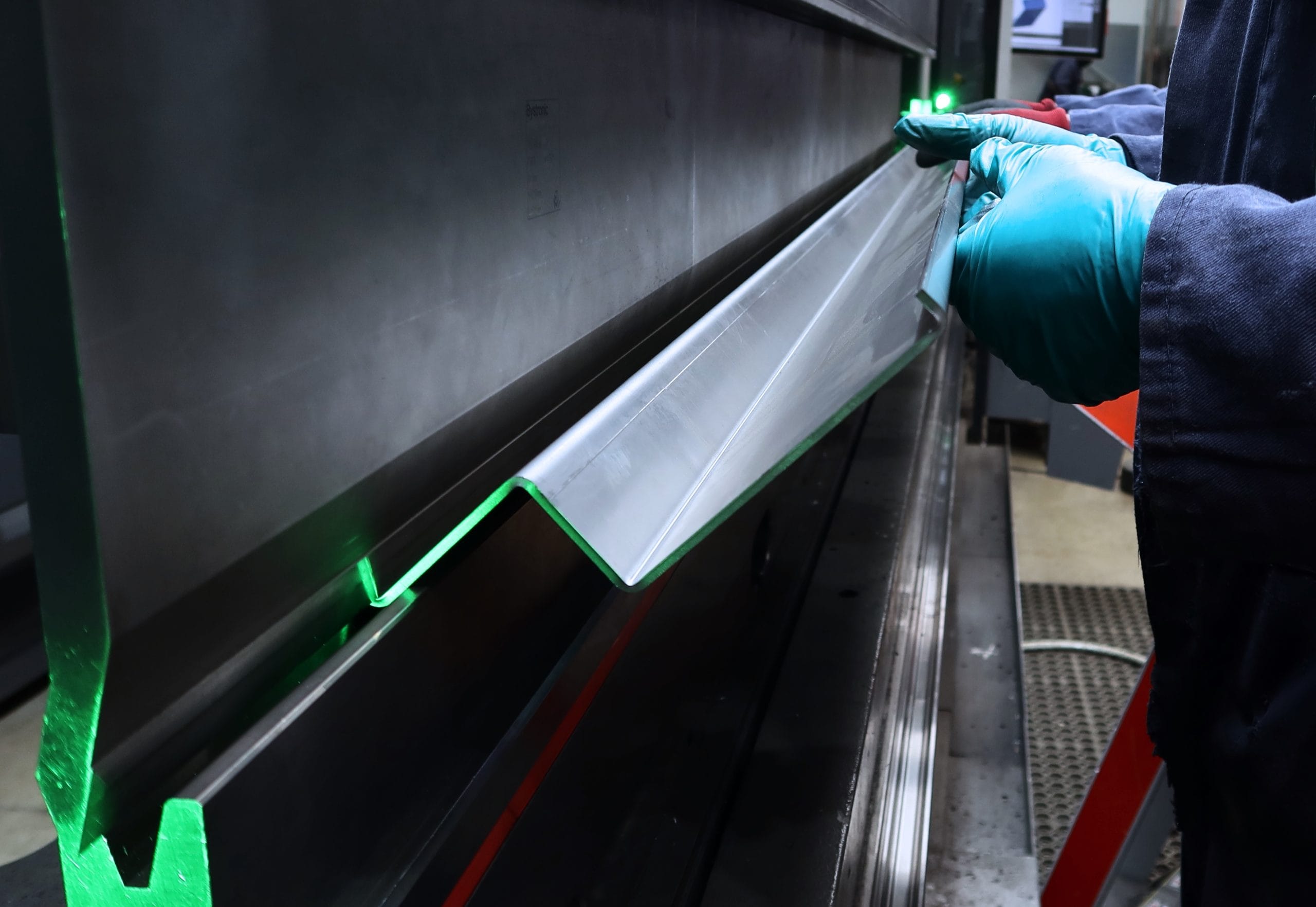 Close-up of sheet metal being bent on a press brake machine with green laser alignment, operated at Riteweld Engineering in Oxford