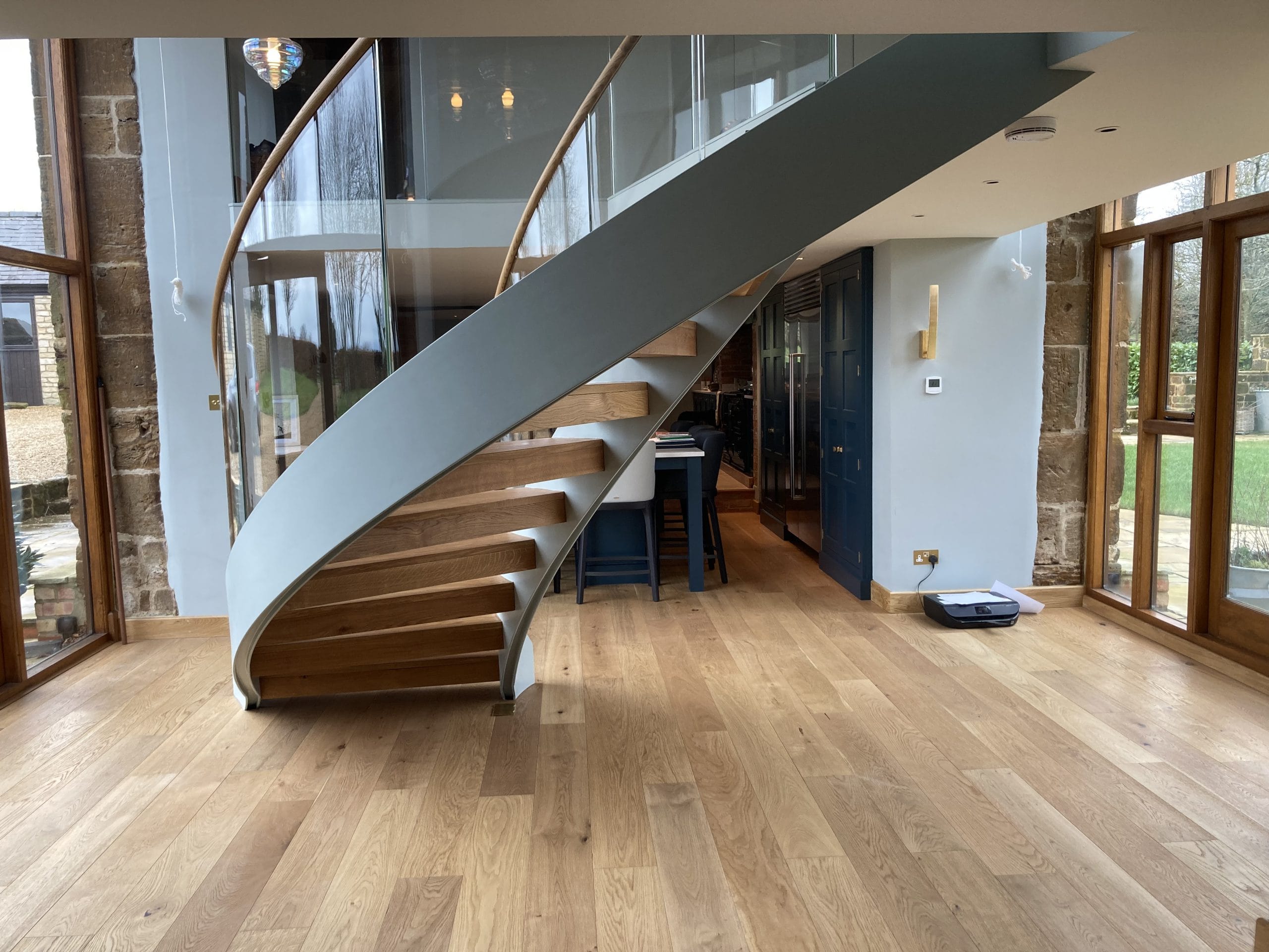 Curved steel staircase with glass balustrade, timber treads, and timber handrails, installed in a modern interior by Riteweld Engineering.
