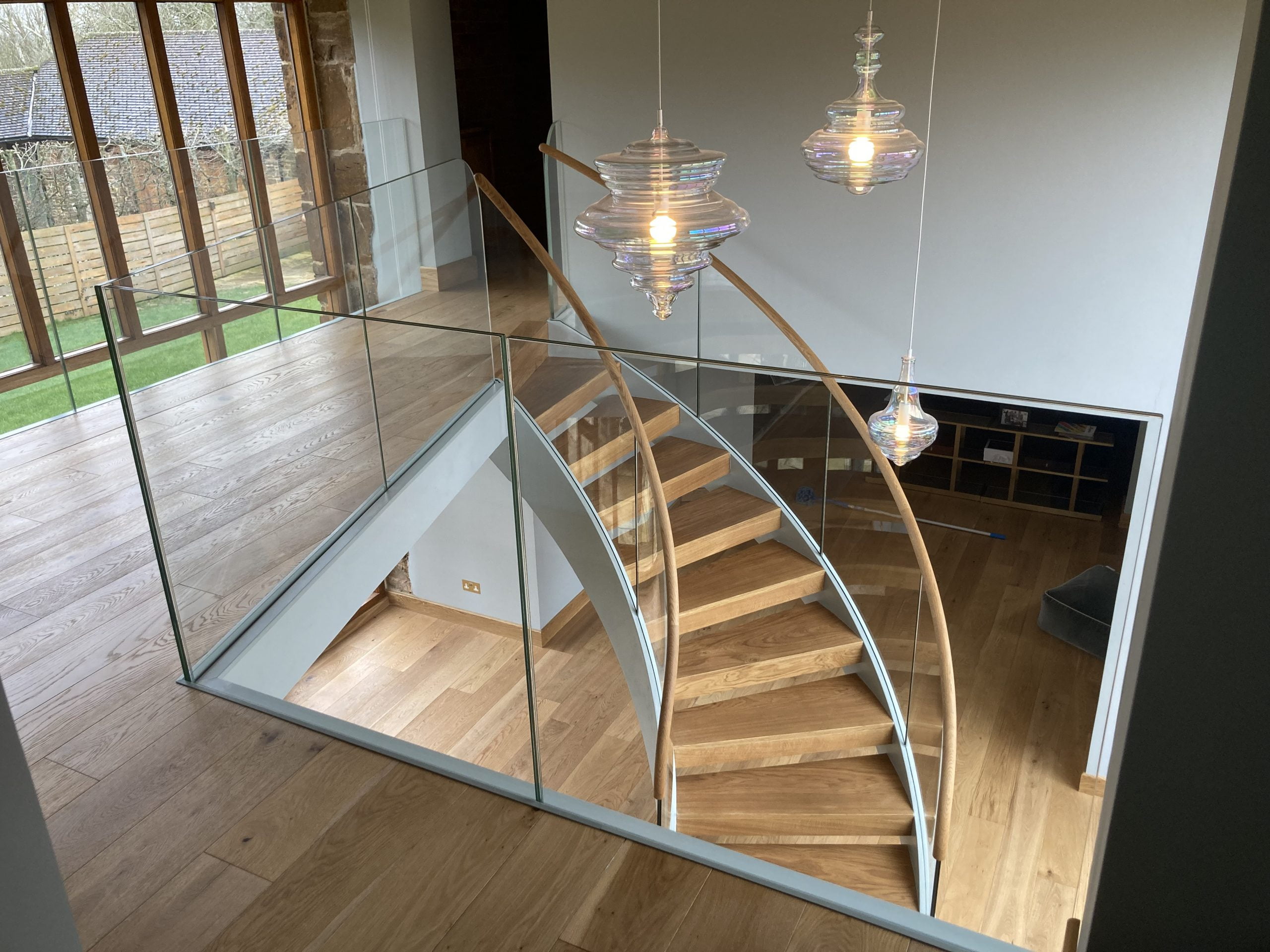 Overhead view of a curved feature staircase with timber treads and handrails, glass balustrades, and a steel structure, installed by Riteweld Engineering in a modern interior.
