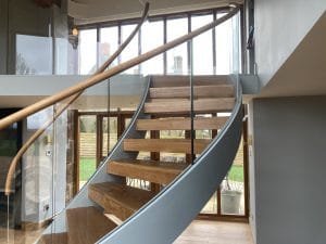 Curved staircase with steel stringers, glass balustrades, and timberland rail and treads, installed in a modern interior by Riteweld Engineering.