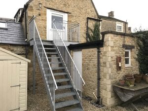 External steel staircase with handrails leading to an upper-level door and access platform, installed by Riteweld Engineering on a stone residential building.
