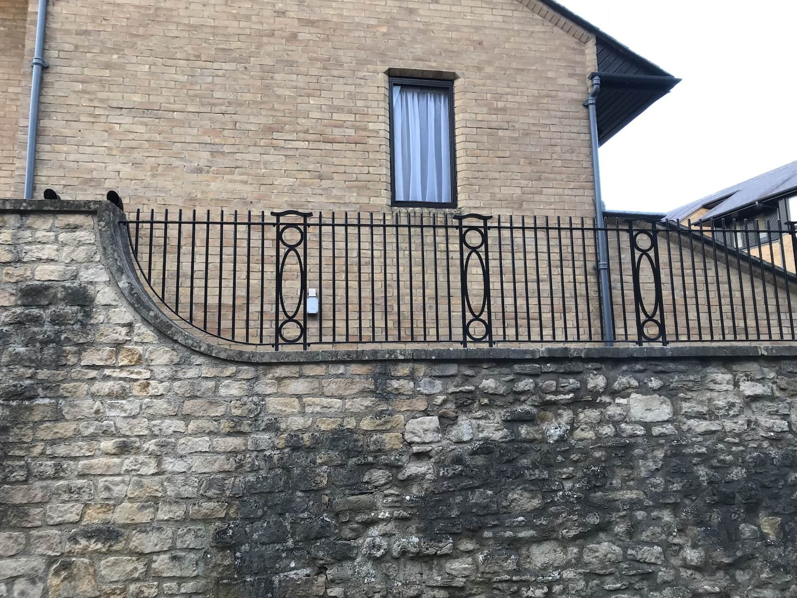 Decorative steel railings with curved detailing installed on top of a stone boundary wall outside a residential property, by Riteweld Engineering.