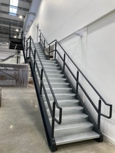 Industrial steel staircase with safety handrails installed along a white interior wall, fabricated and fitted by Riteweld Engineering.