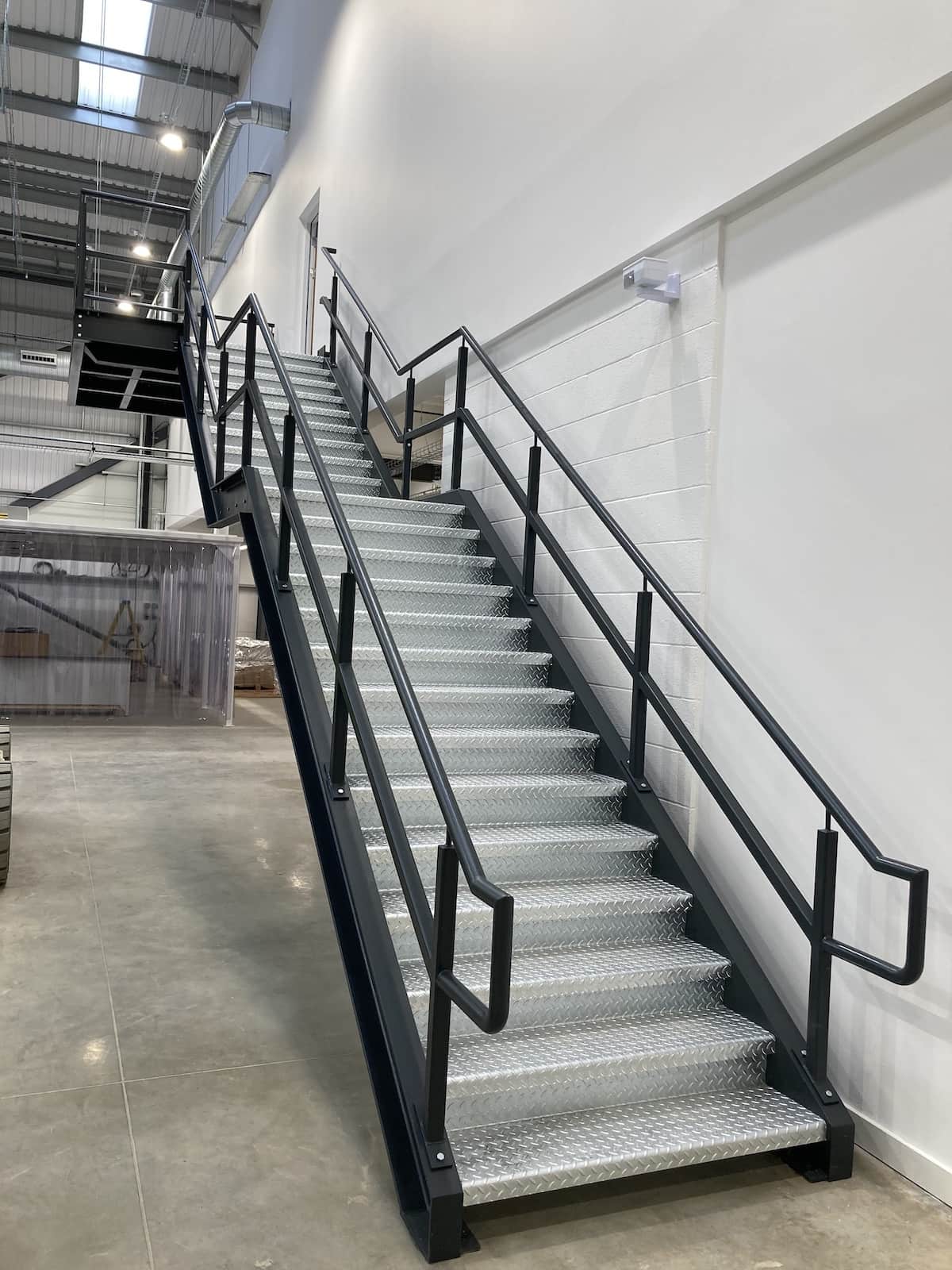 Industrial steel staircase with safety handrails installed along a white interior wall, fabricated and fitted by Riteweld Engineering.