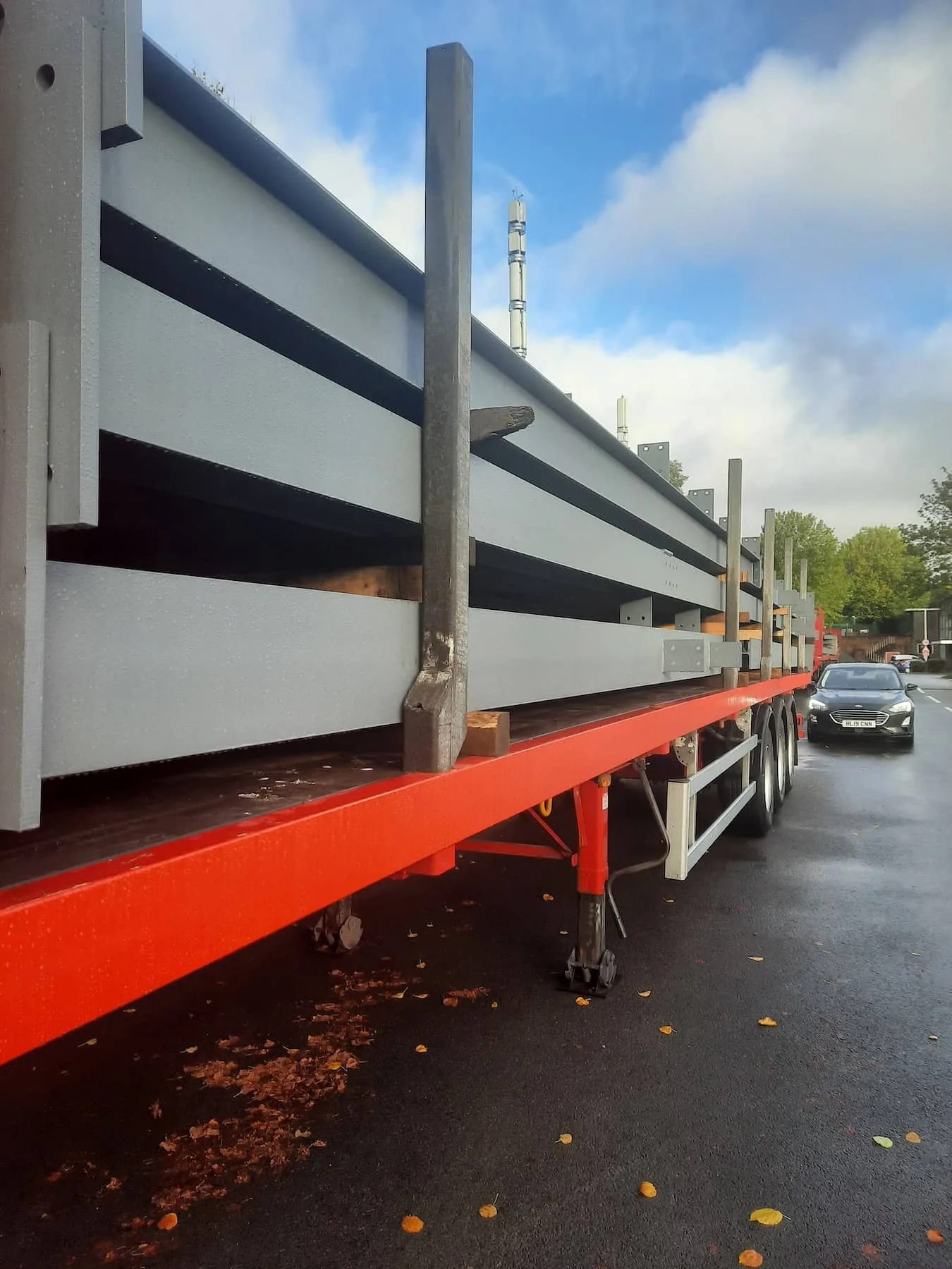 Painted structural steel beams stacked and secured on a red flatbed trailer, ready for transport by Riteweld Engineering.