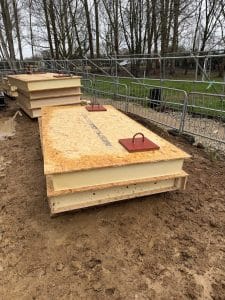 SIPs roof panels with PIR insulation and OSB faces fitted with steel lifting plates, ready for crane installation on a residential construction project.