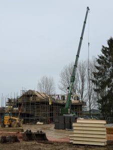 Mobile crane lifting structural elements and SIPs roof panels during roof installation on a residential construction project.